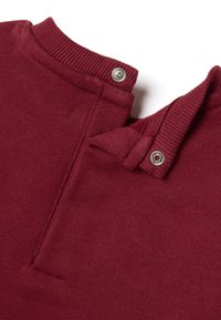 Burgunderfarbenes Strickgewebe mit einer strukturierten Oberfläche, das über einen Druckknopfverschluss am Kragen und ein gefaltetes Design verfügt.