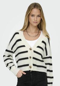 Cárdigan de punto con tejido blanco y rayas negras horizontales, mangas largas, cuello redondo y tres grandes botones en el frente.