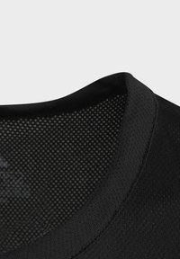 Camisa deportiva negra con un cuello texturizado y tela de malla transpirable, con patrones de puntos visibles en la capa interna.