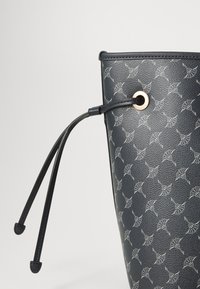 Navy bucket bag featuring a subtle patterned design and a drawstring closure with a gold-toned eyelet and black cords.