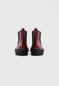 Burgundinpunaiset nahkaiset nilkkurit, joissa mustat joustavat sivupaneelit ja mustat paksut kumipohjat. Varustettu kantalenkillä helpottamaan pukemista.