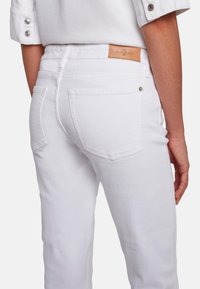 Hvide denim jeans med en glat tekstur, der har baglommer og en lysebrun læderlap på taljen. Inkluderer metalhardware detaljer.