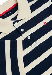 Marinblå och krämfärgad randig polo tröja, tillverkad av bomull med klassisk krage, har tre knappar och en röd broderad logo.