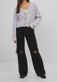 Lys lavendel strikket cardigan med en dyb V-udskæring, prydet med tre træknapper. Sammen med slidte sorte brede jeans.