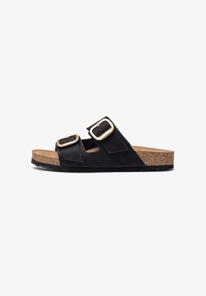 Les sandales à glissière en suede noir présentent deux sangles réglables avec des boucles dorées, une semelle en liège et une semelle en caoutchouc noir texturé.