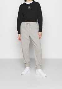 Felpa nera corta con logo Nike bianco, abbinata a pantaloni della tuta grigio chiaro con fondo rastremato e sneakers bianche. Tessuto liscio, polsini elastici.