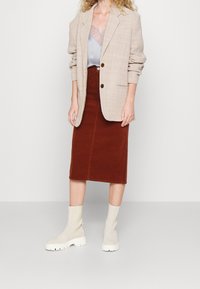 Blazer de cuadros beige claro, top azul claro, falda lápiz color óxido y botines crema con suelas gruesas. Telas suaves y diseño ajustado.