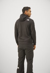 Felpa nera con cappuccio dal design aderente, texture morbida e logo sulla spalla, abbinata a pantaloni neri coordinati con loghi.