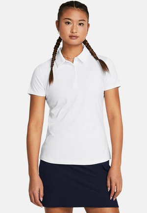 Weißes Polohemd mit Kragen und drei Knöpfen, aus glattem Stoff gefertigt. Kombiniert mit einem marineblauen Rock; das Modell hat geflochtene Haare.