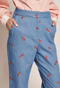 Svetlo modri kavbojki z vezeninami rdečih češenj in zelenimi listi, ki imajo stranske žepe in oprijet pas.