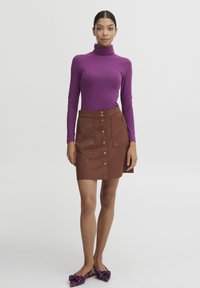 Lilla turtleneck-top kombineret med en brun ruskindsnederdel med frontknaplukning og sidelommer med lynlås. Sorte og lilla mønstrede flade sko.
