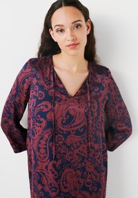 Bordeauxfarbene und marineblaue gemusterte Bluse mit V-Ausschnitt, langen Ärmeln, komplexem Paisley-Muster und glatter Stofftextur.