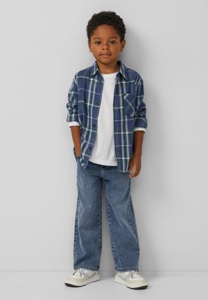 Blauwe geruite overhemd met knopen over een wit T-shirt, gecombineerd met blauwe denim jeans en witte sneakers. Het overhemd heeft een borstzak.