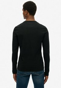 Zwarte lange mouwen shirt van katoen, met een ronde hals en een aansluitend ontwerp. Gekenmerkt door een minimalistische stijl, gedragen met blauwe spijkerbroeken.