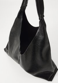 Svart läder axelväska med en avslappnad design, mjuk textur, öppen topp och bred handtag för enkel bärbarhet.