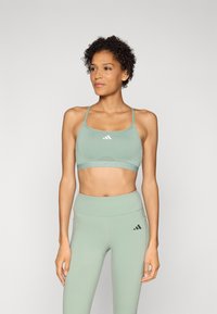Lysegrønn sports-bh med justerbare stropper og utskjæringsdesign, parret med matchende høyt midje leggings som har svarte logo-detaljer.