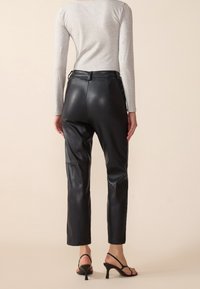 Pantalon en cuir noir à coupe ajustée, doté d'une taille haute, d'une texture lisse et de coutures discrètes. Associé à des talons fins noirs.