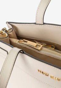 Beige leren handtas met een gouden rits en hardware, zwarte afwerking, en interieurvakken, waaronder één vak met rits.