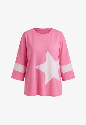 Top roz rozî cu mâneci trei sferturi supradimensionat, cu o stea albă în față și dungi albe în jurul mânecilor.