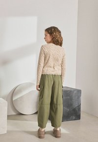 T-shirt beige à manches longues avec des pois roses et une bordure en dentelle, associé à un pantalon cargo ample vert olive. Chaussures à plateforme marron.