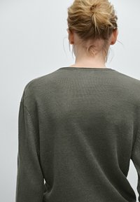 Grøn strikket sweater med løs pasform, rund halsudskæring og ribstrikket detalje på ærmekanter og kant. Synlig tekstur fra stofvævningen.