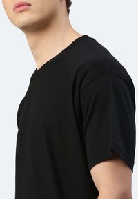 Maglietta nera in cotone con scollatura a girocollo, maniche corte e design aderente, che mette in mostra una texture liscia e uno stile minimalista.