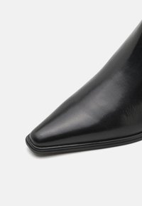 Chaussure en cuir noir à bout pointu avec une finition lisse, affichant une silhouette élégante et un design minimaliste avec une semelle en caoutchouc discrète.