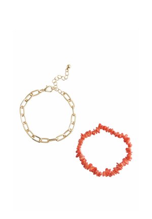 Goldkette Armband mit großen Gliedern und Verschluss sowie dehnbares Armband aus kleinen unregelmäßigen roten Korallenperlen vor weißem Hintergrund.