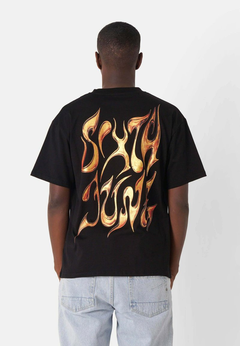 Camiseta de algodón negra con un gran diseño de llama dorada estilizada en la parte posterior. Mangas cortas y un corte relajado.