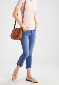 Světle růžový krátkosrstý top s krátkým rukávem, modré džíny po kotníky, béžové kožené mokasíny s třásněmi a hnědá přes rameno taška.