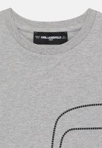 Grå bomulls-T-shirt med ribbad rundhals och en svart prickad linjedesign på framsidan. Märkesetikett synlig på insidan av kragen.