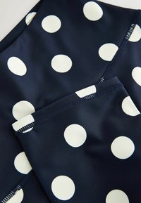 Tissu bleu marine à pois blancs montrant les bords cousus et les sections pliées, mettant en valeur les détails de la texture et du motif.