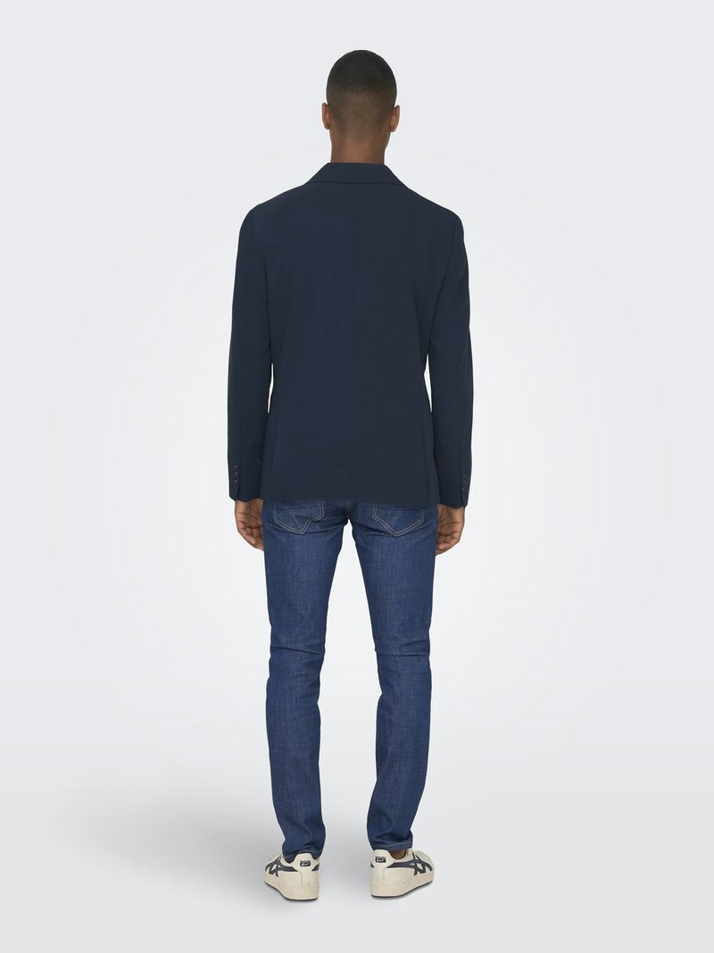 Giacca navy con una vestibilità su misura, abbinata a jeans blu e sneakers bianche, vista da dietro, evidenziando il design delle spalle e della giacca.