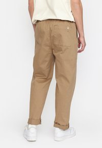 Pantalones marrones de corte entallado hechos de algodón con un ajuste relajado, que incluyen un bolsillo trasero y dobladillos enrollados, combinados con zapatillas blancas.