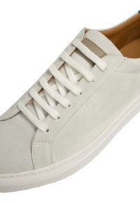 Sneaker in suede grigio chiaro con un design pulito, lacci bianchi e suola in gomma testurizzata. Accentuato da una linguetta beige vicino alla caviglia.