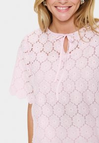 Pink lace top with floral pattern, short sleeves, keyhole neckline, and ribbon tie detailing. Lightweight fabric with a textured finish.