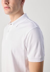 Hvit polo-skjorte med to-knapps placket, mykt bomullsmateriale, korte ermer og subtilt opphevet "BOSS"-logo på brystet.