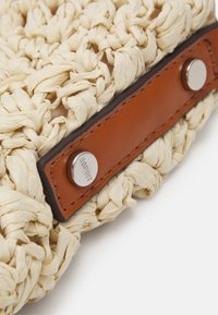 Borsa in paglia intrecciata di un beige naturale con accenti in pelle marrone liscia. Presenta una chiusura a scatto circolare in metallo e un'esterno testurizzato e intrecciato.