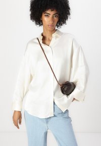 Krem satin oversized skjorte med krage og knappestolpe, kombinert med lyseblå denimjeans og en liten brun lærveske.