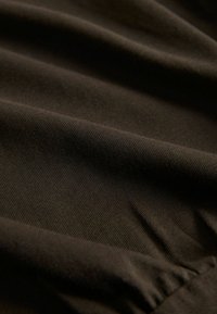 Material maro închis cu nervuri diagonale fine și pliuri moi, creând o suprafață texturată și netedă.