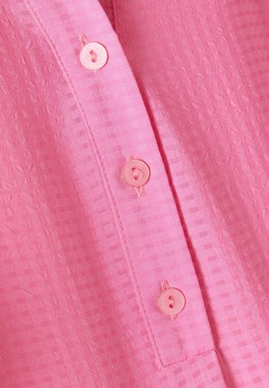 Pink bluse med et tekstureret mønster, med en række af fire matchende knapper langs stængeren og en subtil glans i stoffet.