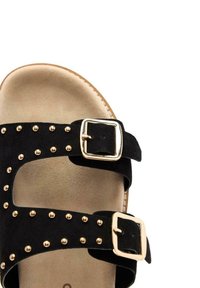 Infradito in suede nero con due ampie cinghie caratterizzate da borchie e fibbie dorate, suola piatta con insole imbottita beige.