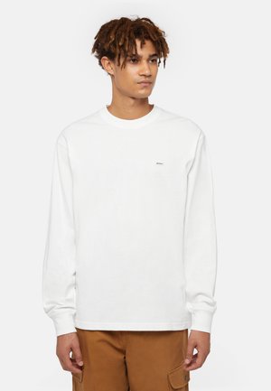 Witte longsleeve T-shirt van katoen, met ronde hals en een klein logo op de borst; gecombineerd met bruine cargobroek.