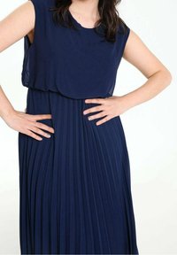 Robe plissée bleu marine avec un col rond et un design sans manches, dotée d'une texture de tissu fluide qui tombe en douceur.