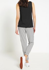 Černý bezrukávový top spárovaný s bílými kalhotami s vzorem. Kalhoty mají geometrický design, nosí se s bílými teniskami.