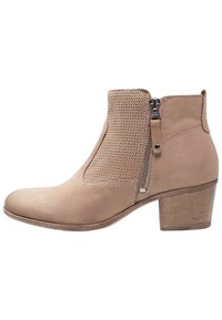 Beežit saapikas, millel on ümmargune nina, tekstuuriga kudumiskeelega ülemine osa, külgcip, ja madal puidust plokknina.