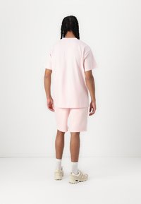 Helles rosa Baumwoll-T-Shirt und passende Shorts, entspannte Passform, glatte Textur, kombiniert mit beigen Sneakers und weißen Socken.