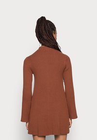 Robe en tricot côtelé marron avec un corsage ajusté et des manches évasées, dotée d'un col rond et d'un ourlet légèrement évasé.