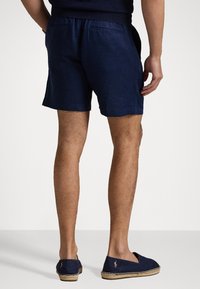 Marina linnebyxor med avslappnad passform, utrustade med dragsko i midjan och två bakfickor. Bärs med marinkolorede espadriller.