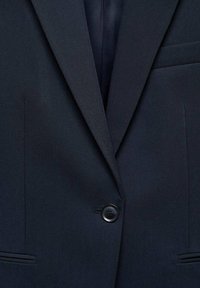 Blazer bleu marine foncé avec revers crantés, fermeture à un bouton noir et poches passepoilées de chaque côté.